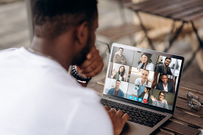Video call. Online business meeting. A successful African American freelancer communicates via video conference with his colleagues using a laptop while sitting in a cafe. On his laptop screen are nine other participants on the Zoom conference
